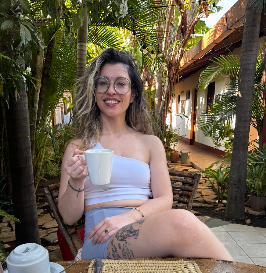Laura smiling with a coffee mug in a lush tropical courtyard